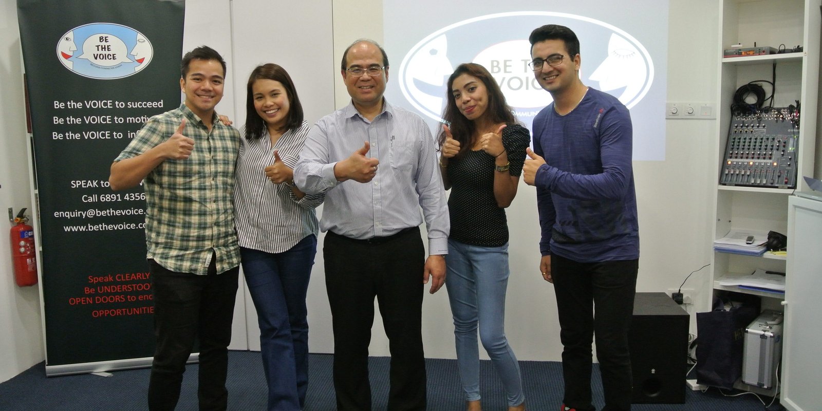 A group of people smiling and giving thumbs up, promoting Be the Voice Academy in Singapore.